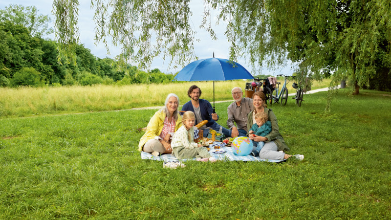 Familie bei einem Picknick im Park unter einem blauen Schirm
