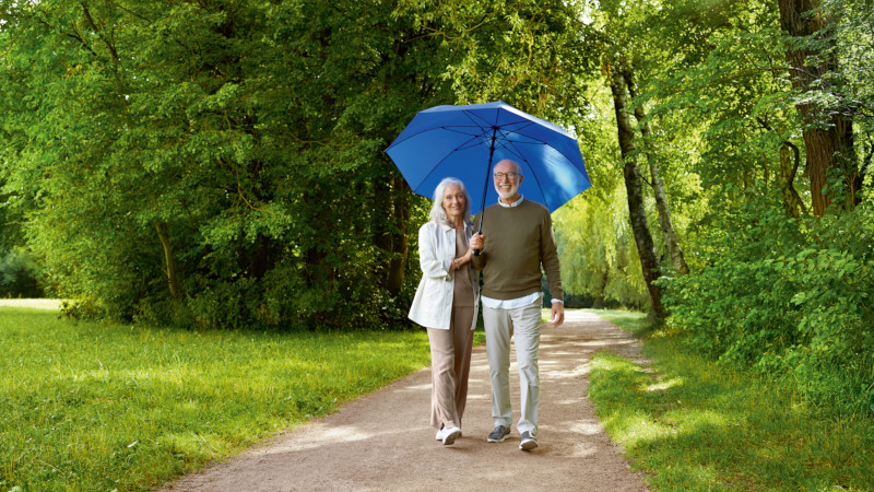 Paar beim Spazieren um Wald unter einem blauen Schirm